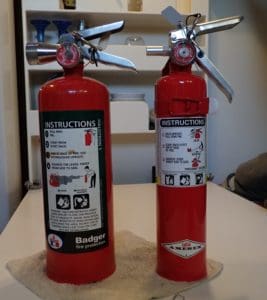 Two fire extinguishers from Rob MacFarlane’s boat Tiger Beetle with sturdy metal handles and nozzles. 