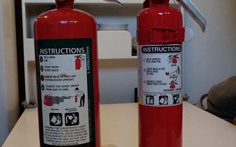 Two fire extinguishers from Rob MacFarlane’s boat Tiger Beetle with sturdy metal handles and nozzles.