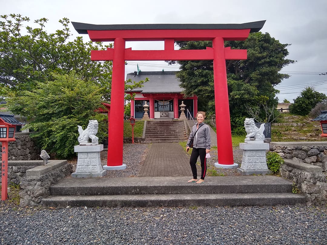 Ginger admires a torii gate and its flanking komainu at a Shinto shrine.